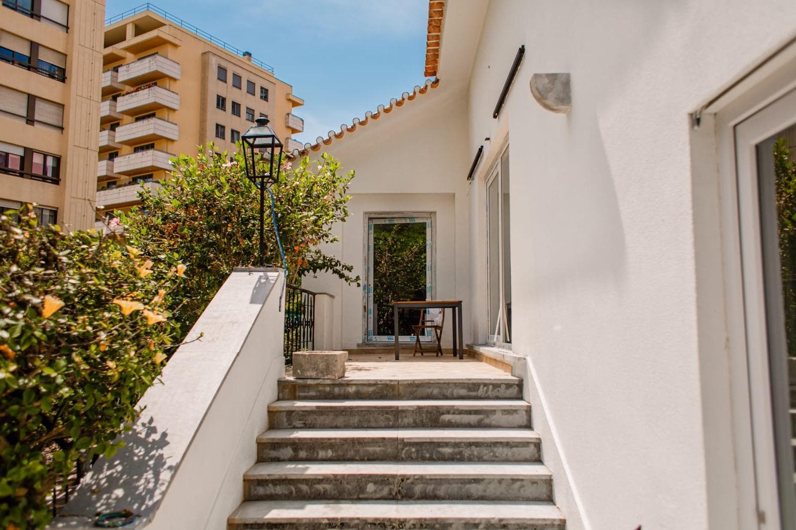 Moradia branca restaurada com cobertura em telha portuguesa, persianas brancas e jardim envolvente.