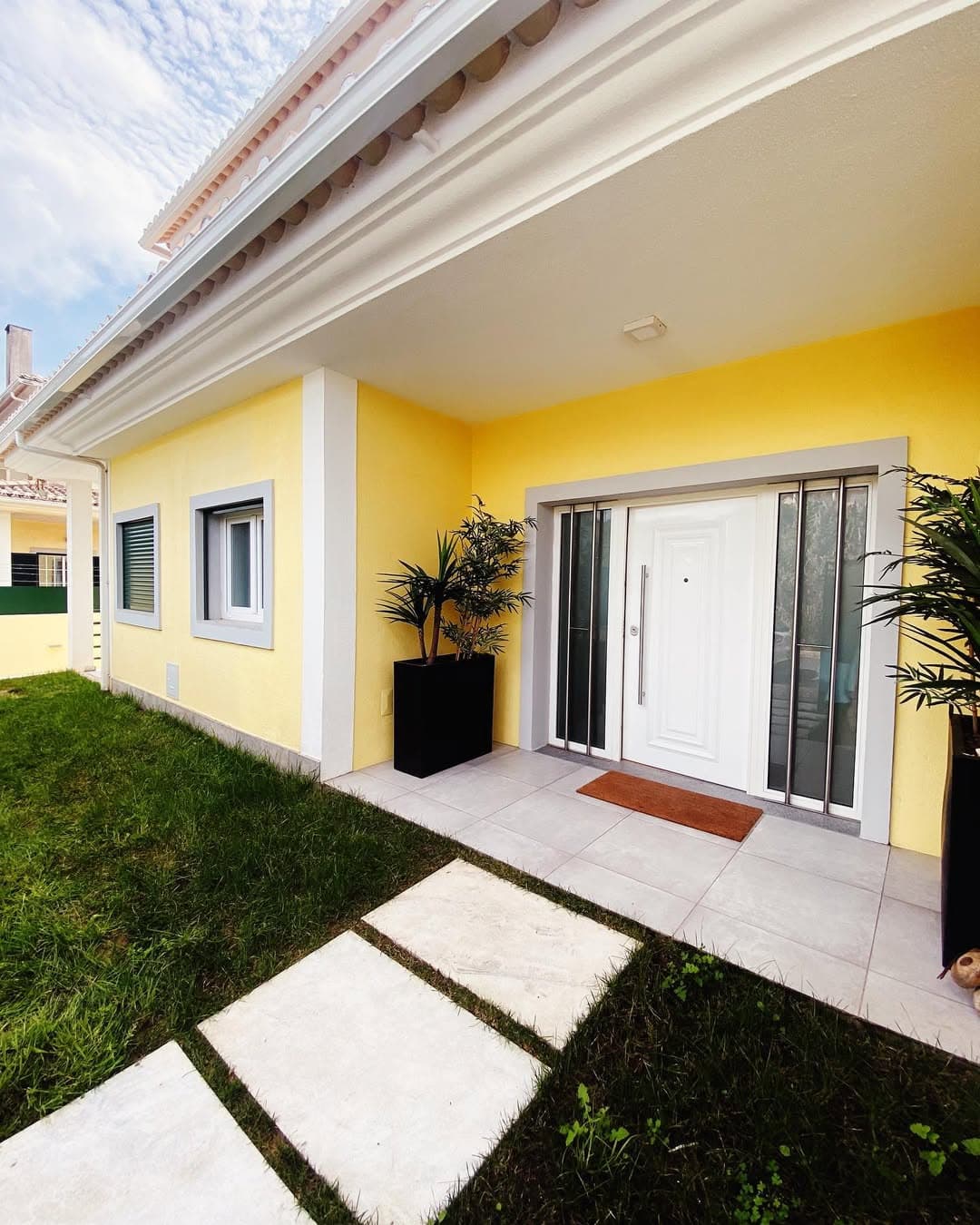 Fachada de moradia remodelada em pintura amarela com porta principal branca e jardim cuidado.
