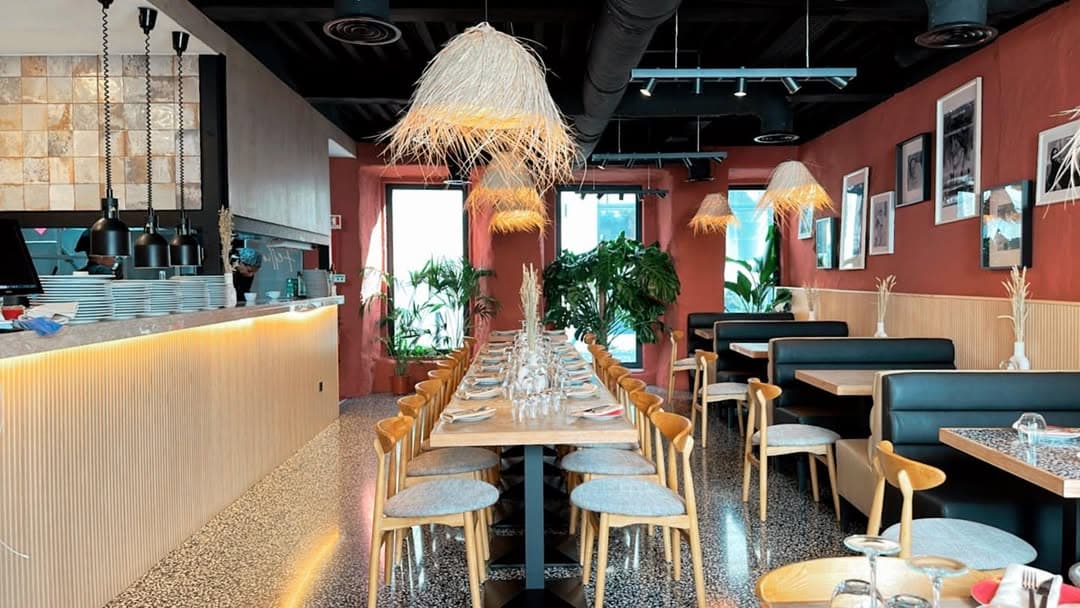 Sala de restaurante com paredes terracotta, candeeiros em rattan e mobiliário em madeira clara.